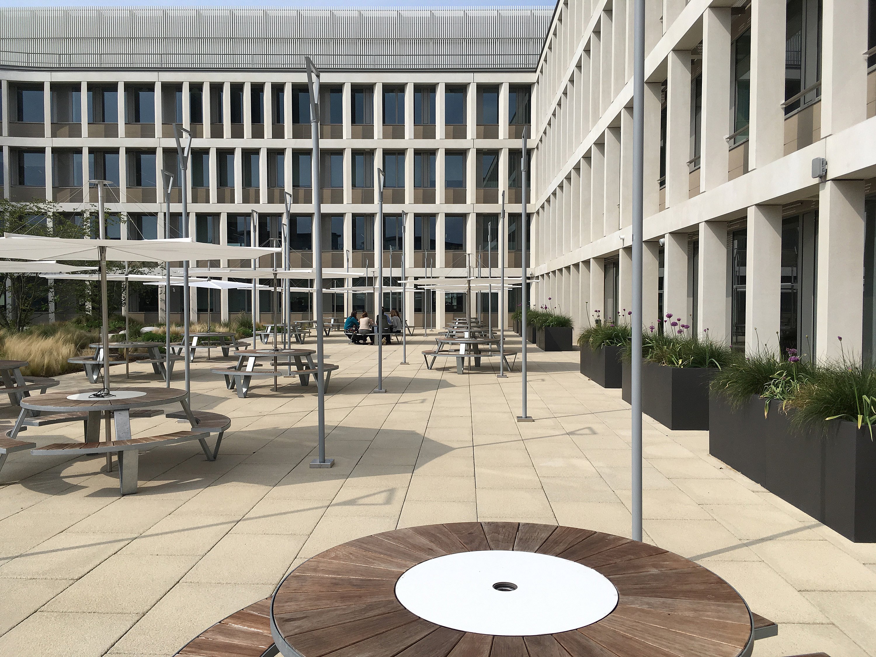Pantagruel picknicktafels met houten stoelen en gegalvaniseerde stalen poten onder Inumbrina-parasols op een geplaveide binnenplaats