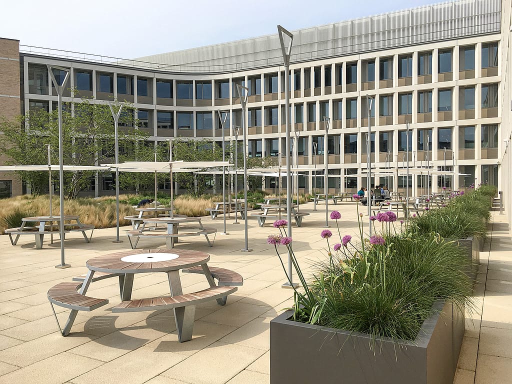 Pantagruel picknicktafels en Inumbrina-parasols onder de gevel van het Cambridge Assessment-kantoor