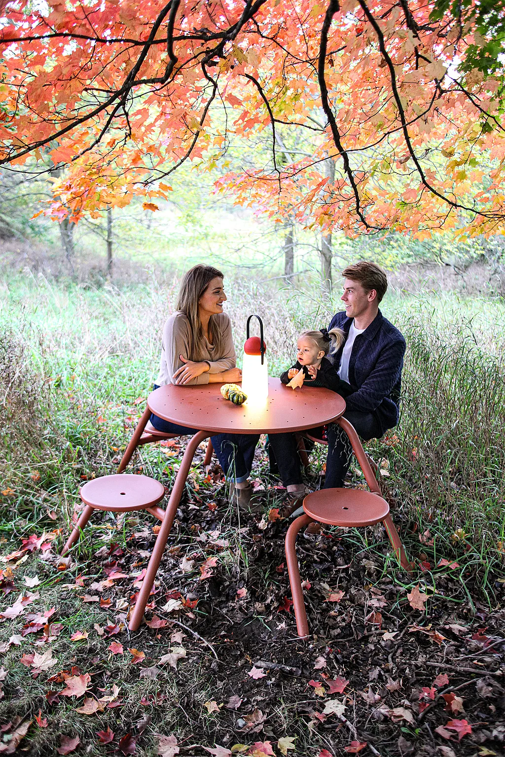 Family gathered around a copper brown Virus table under autumn leaves in tall garden grass