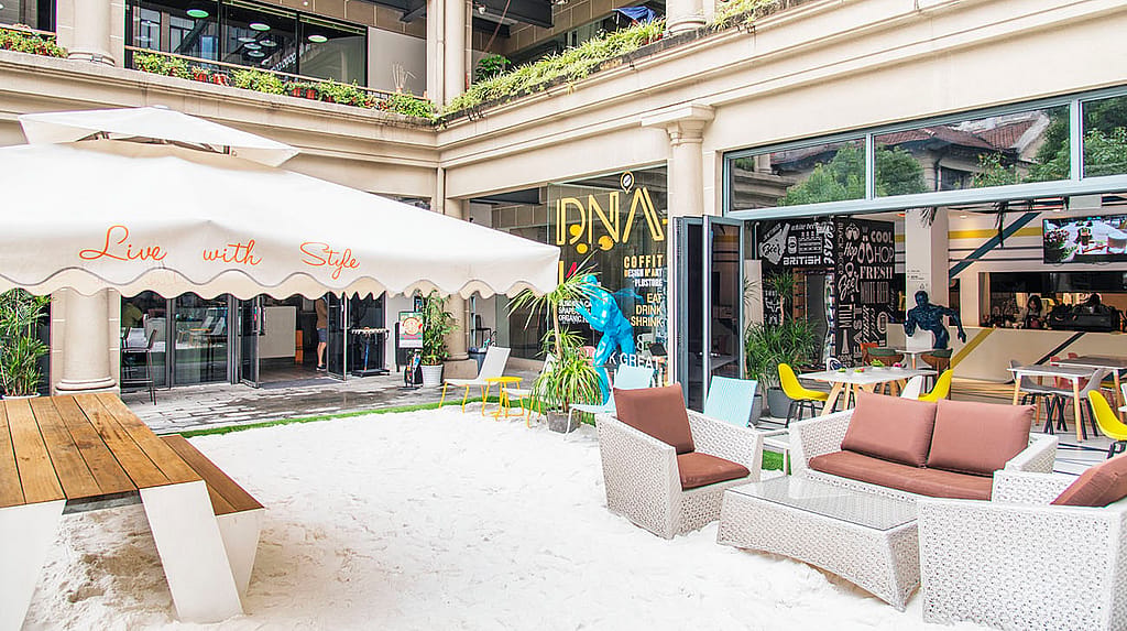 Terrasse de café Sandy avec table de pique-nique Hopper, sièges lounge et chaises colorées à l’extérieur de l’entrée du café