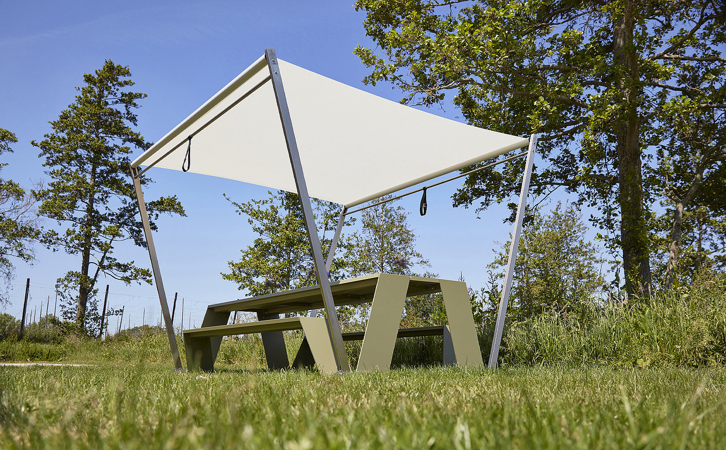 Table de pique-nique Reed green Hopper AA avec des bancs intégrés placés sur l’herbe sous un auvent d’ombre blanc minimaliste recouvert d’une ombre.