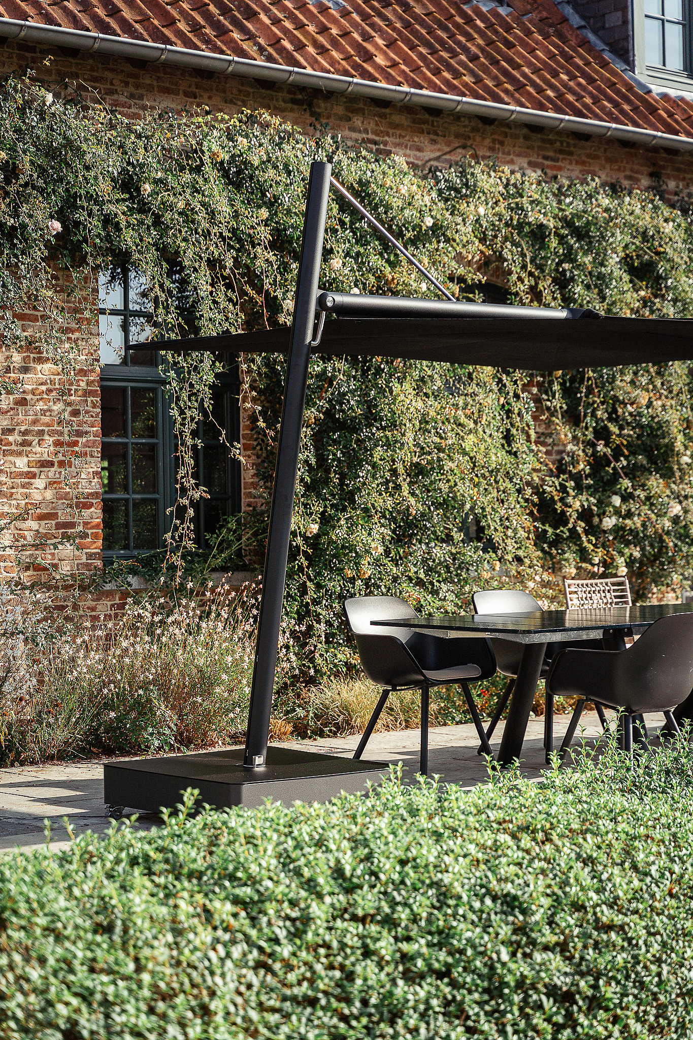 Black Sensu parasol shading a Panigiri Lava table beside a brick farmhouse