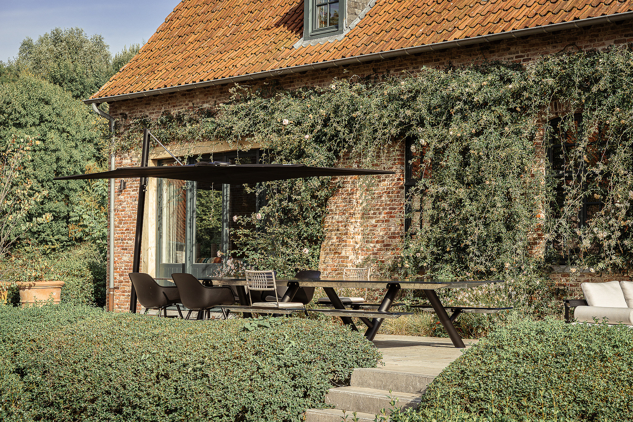Black Sensu parasol shading a Panigiri Lava table beside a brick farmhouse