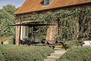 Black Sensu parasol shading a Panigiri Lava table beside a brick farmhouse