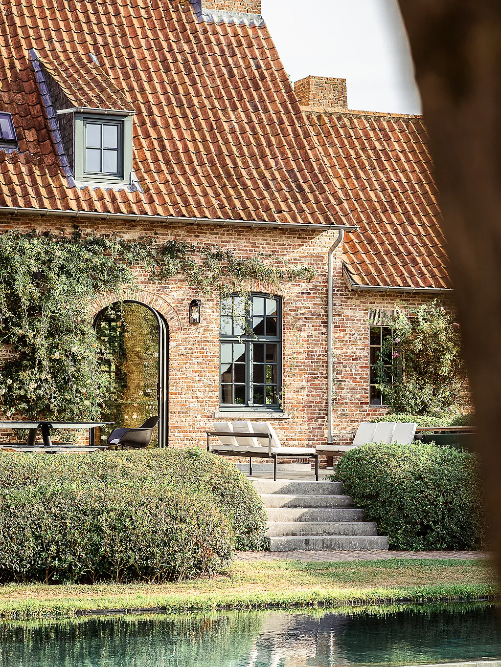 Renovated Belgian farmhouse with Extremis outdoor furniture beside a garden pond