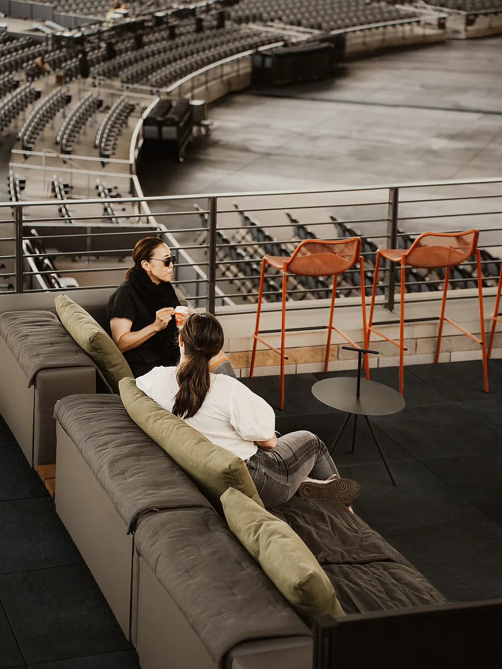 Two guests on an Extremis Walrus outdoor sofa on the Club Terrace, looking out over the bowl at Acrisure Amphitheater