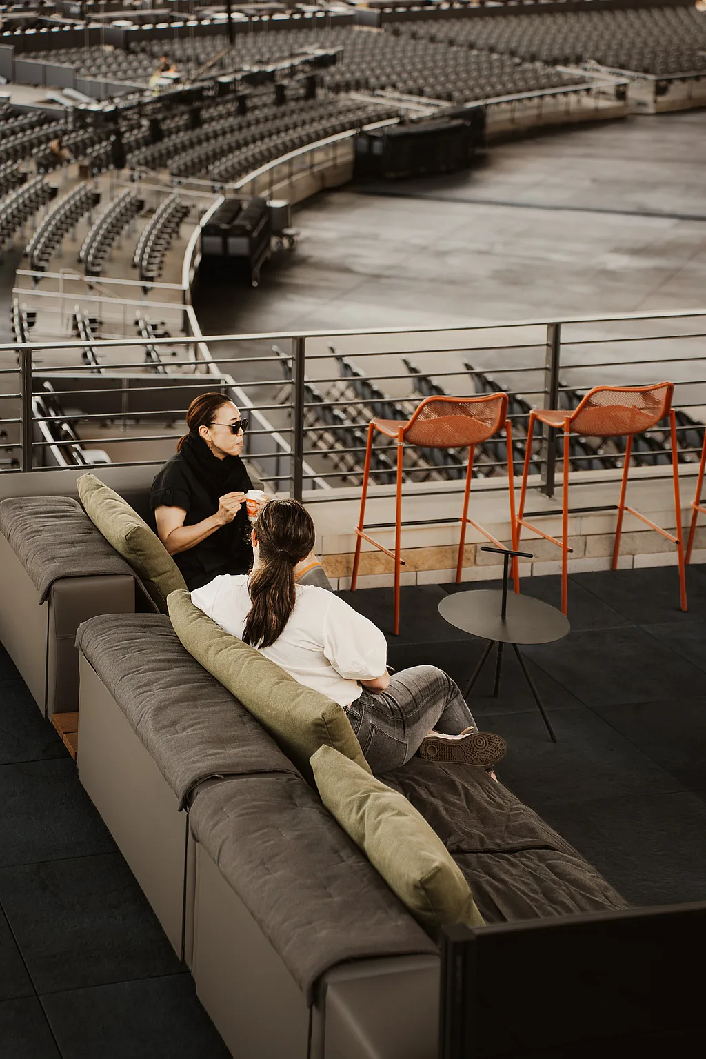 Two guests on an Extremis Walrus outdoor sofa on the Club Terrace, looking out over the bowl at Acrisure Amphitheater