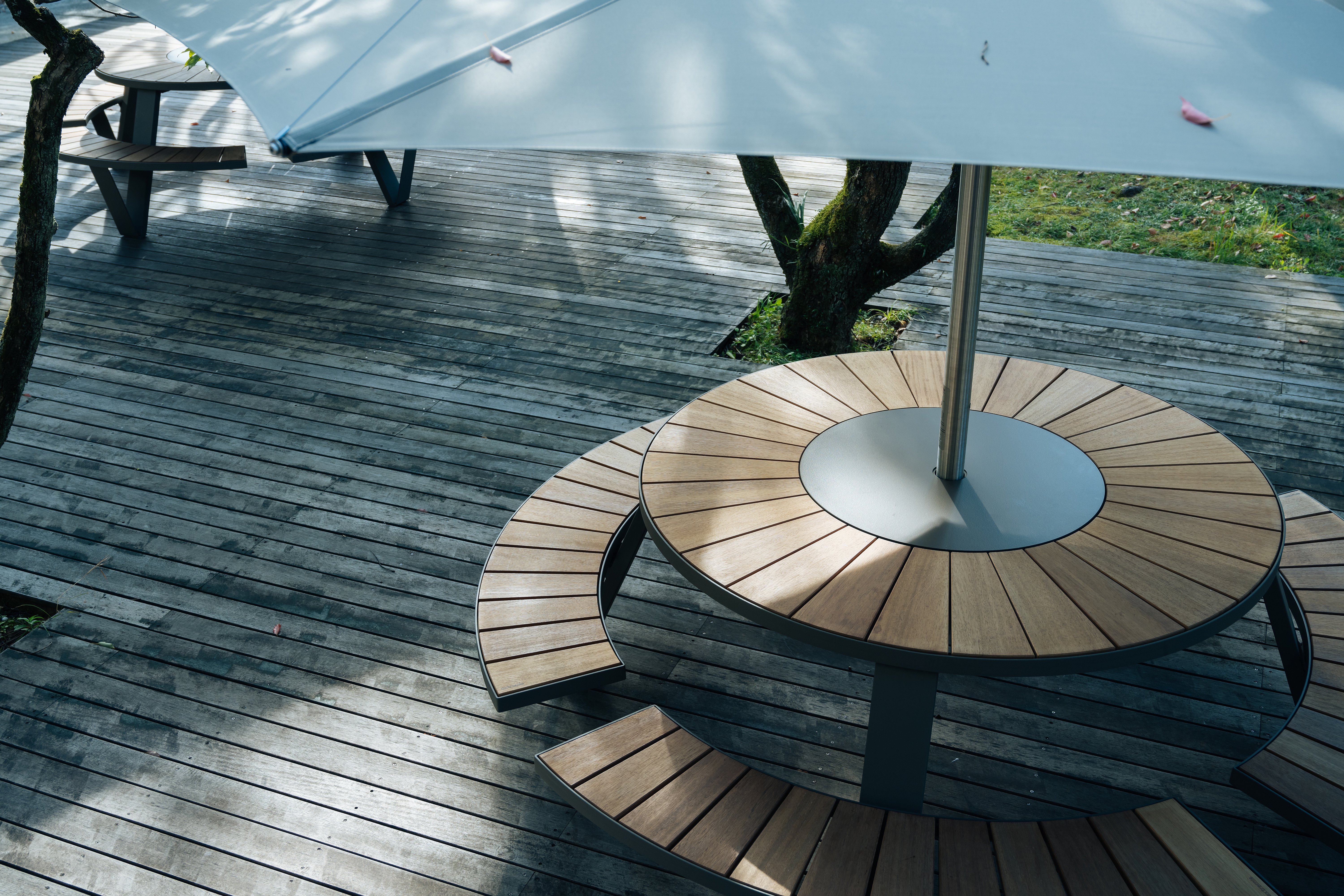 Close-up of a Pantagruel picnic table with wooden benches and central Inumbra parasol