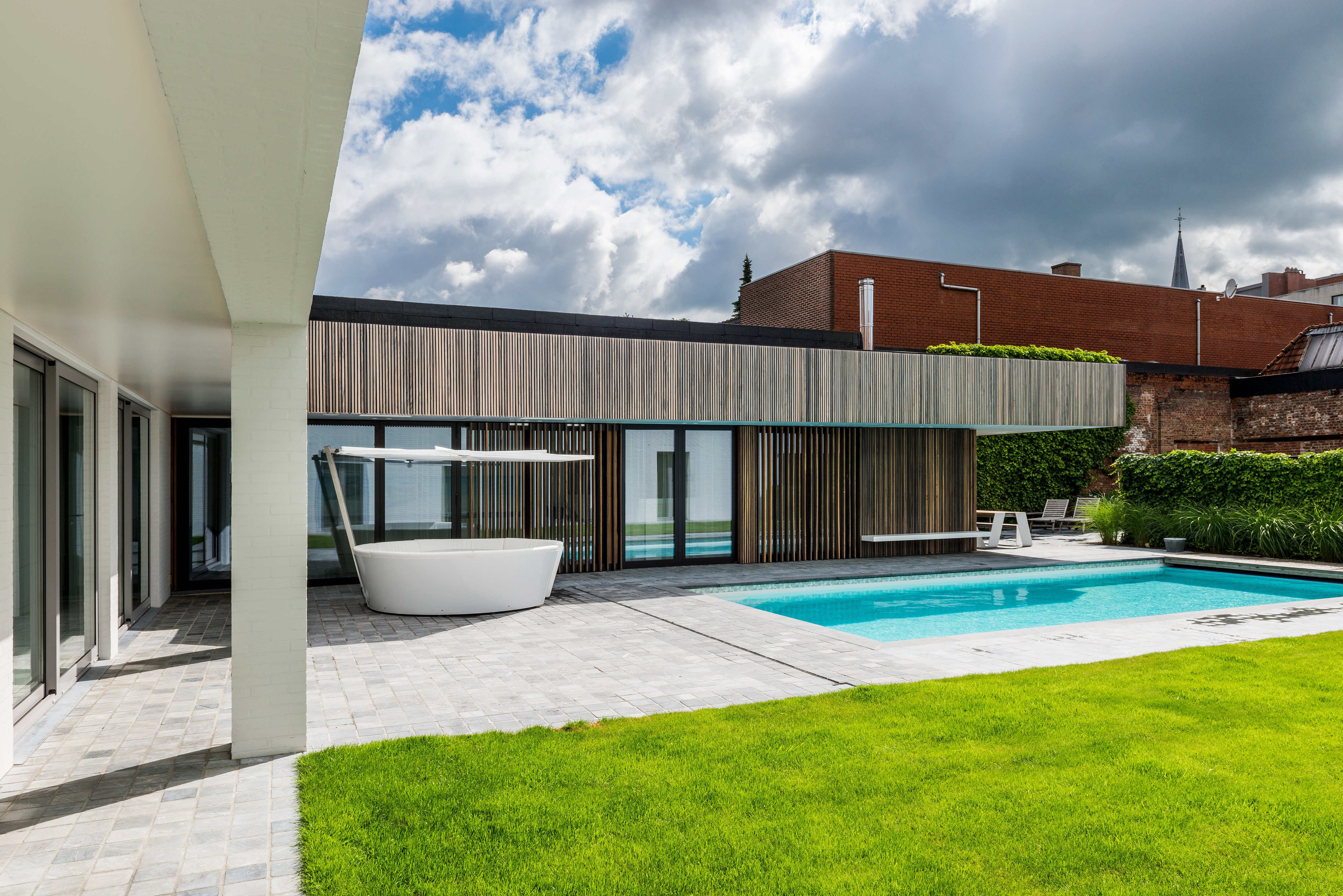 Kosmos circular outdoor sofa with shade beside a swimming pool in a modern courtyard