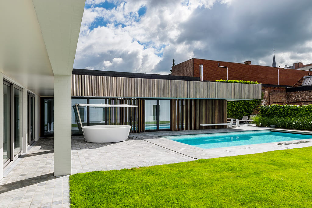 Kosmos circular outdoor sofa with shade beside a swimming pool in a modern courtyard