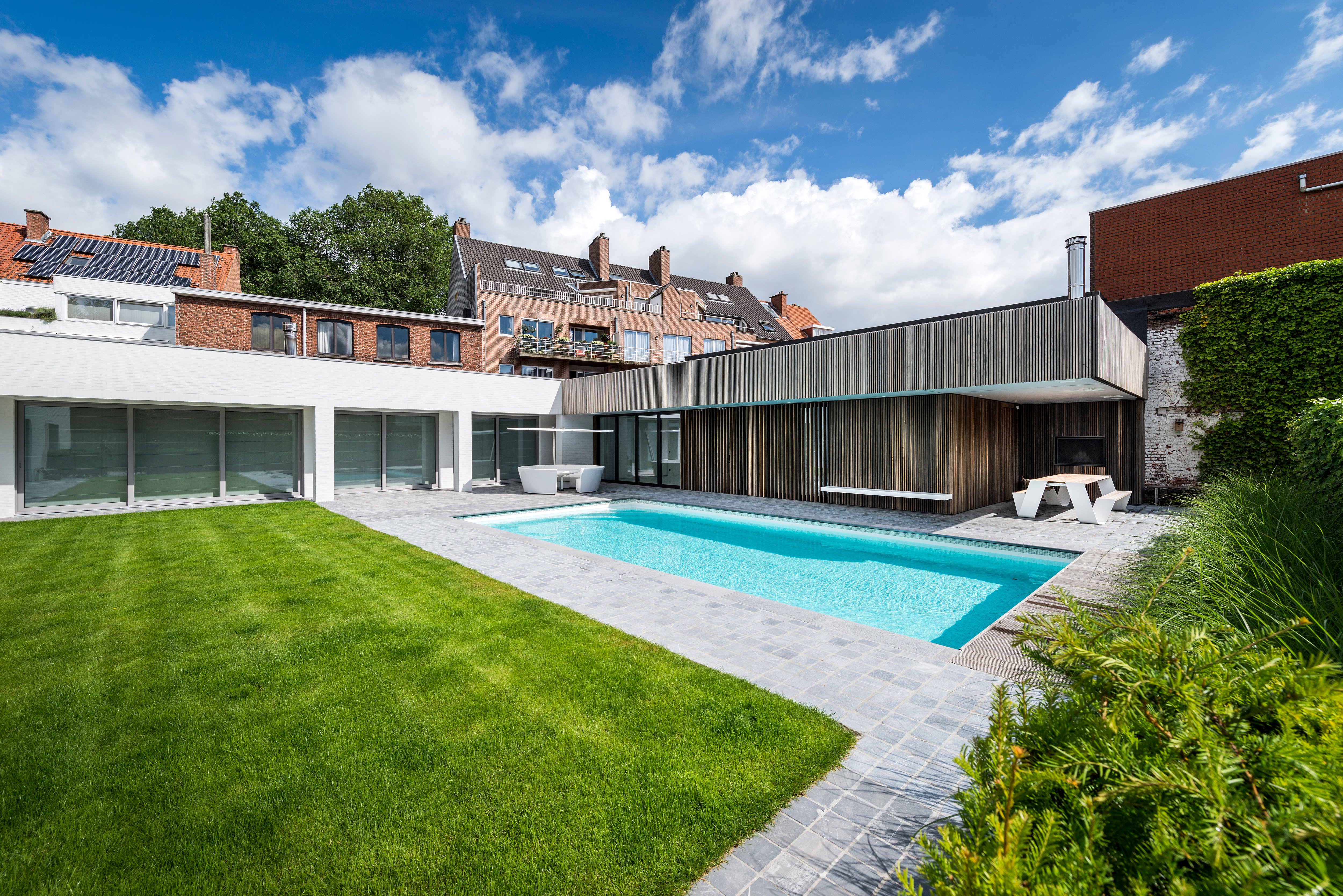 Modern city courtyard with swimming pool, green lawn and Extremis outdoor furniture