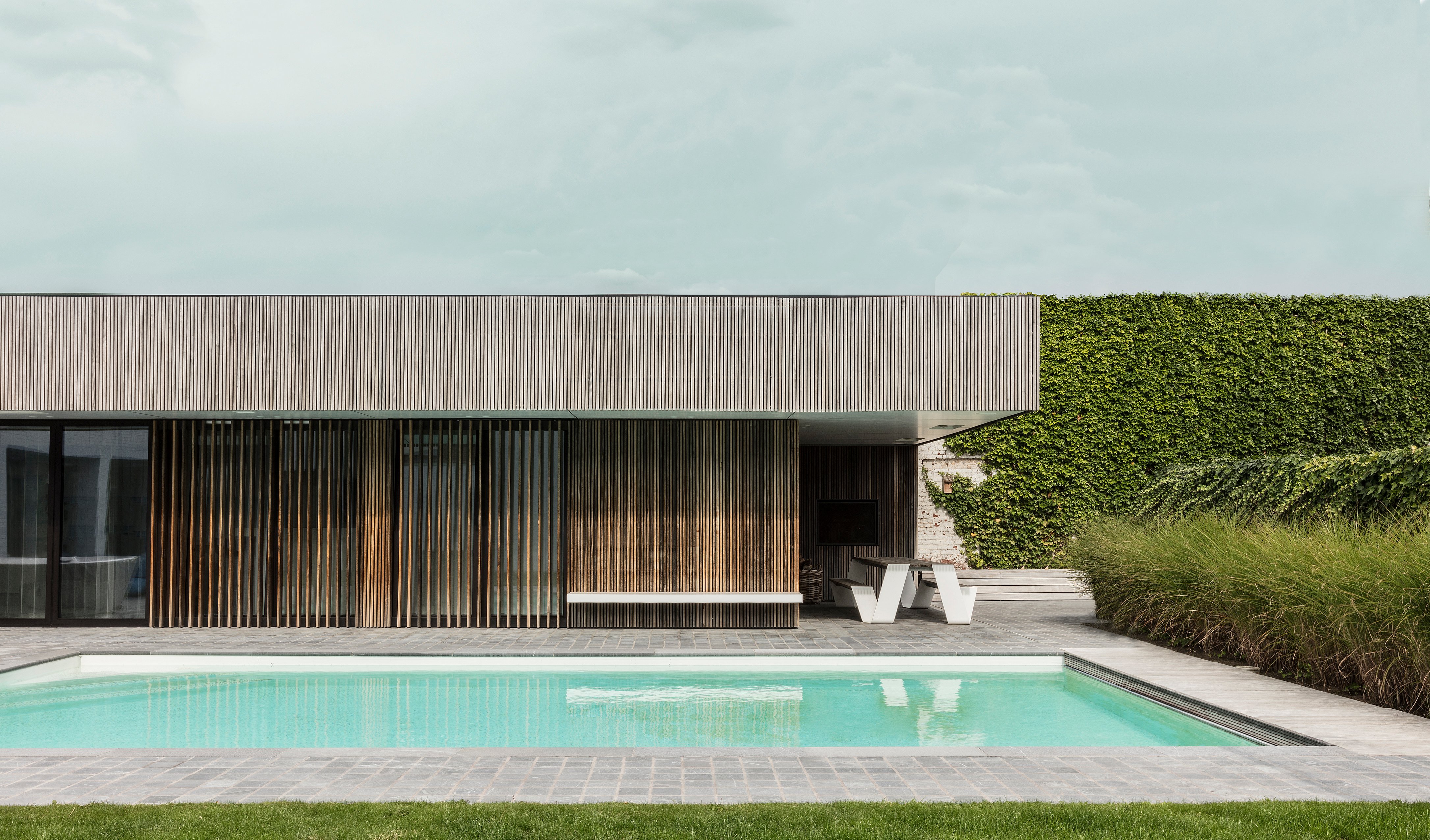 Minimalist pool house with wooden cladding beside a landscaped swimming pool