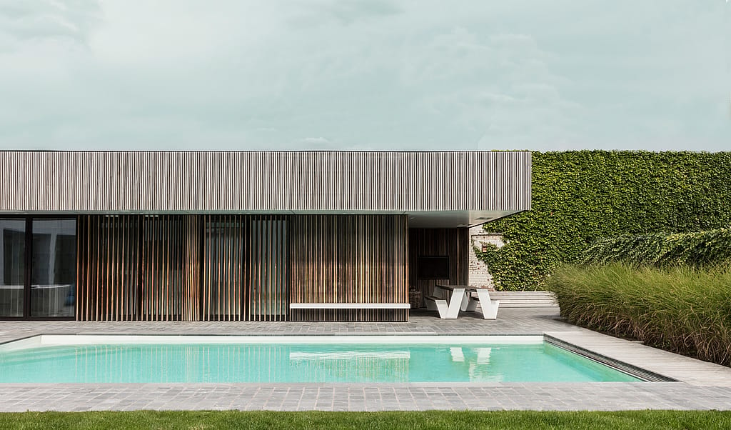 Minimalist pool house with wooden cladding beside a landscaped swimming pool