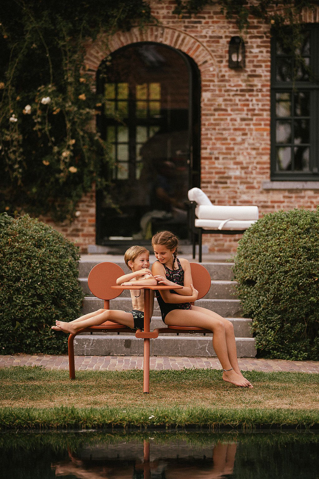 Two children sitting together on a Bistroo seat in the farmhouse garden