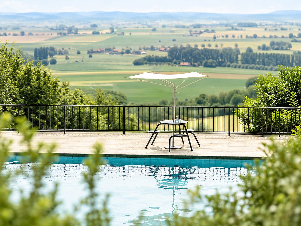 Green Virus table with Acacia shade on a sunny pool terrace, facing a rectangular pool bordered by lush greenery and a vertical wood screen.