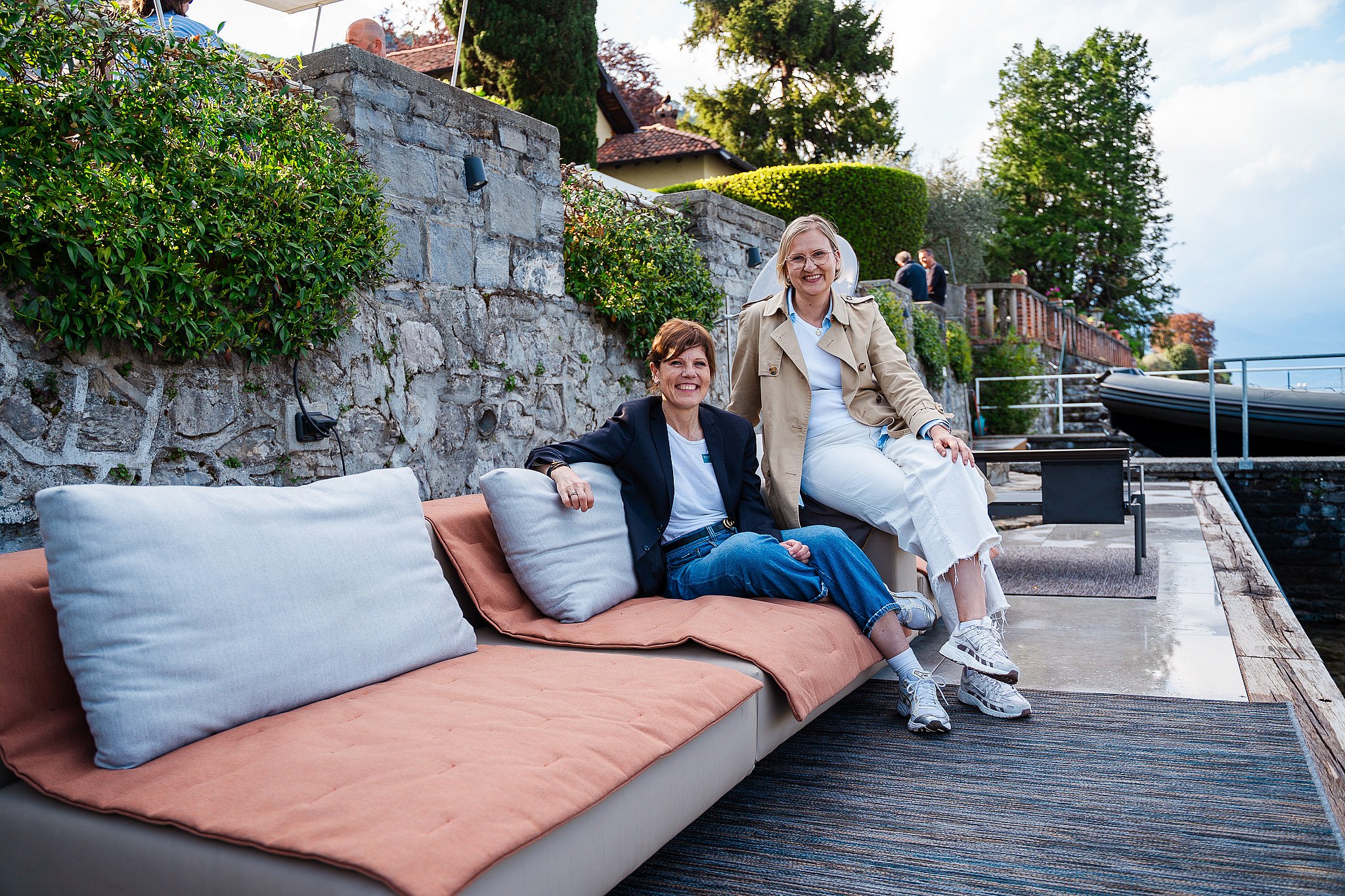 Two guests relaxing on the Extremis Walrus sofa with cushions on the lakeside terrace