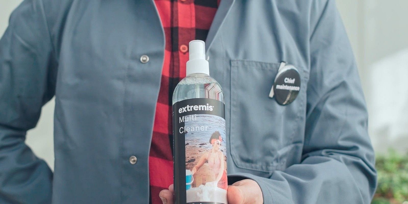 Hand holding a bottle of Extremis Multi Cleaner, the spray used to clean HPL furniture.